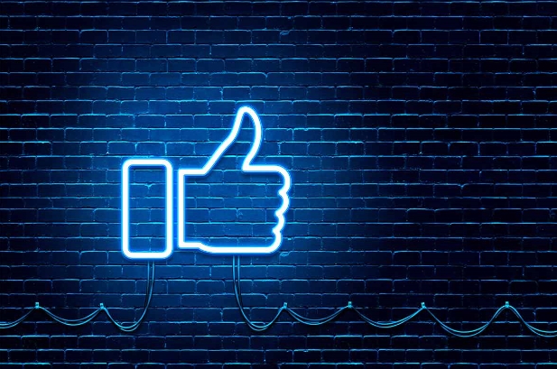 Blau leuchtendes Neonschild von einem Facebook-Daumen vor einer Wand