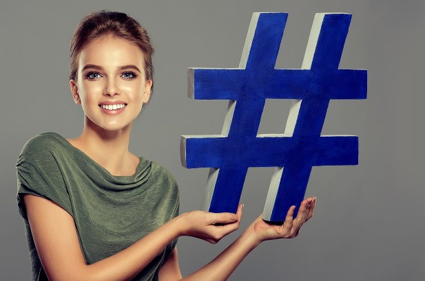 eine junge frau in gruenem tshirt mit einem blauen großen hashtag schaut laechelnd in die kamera