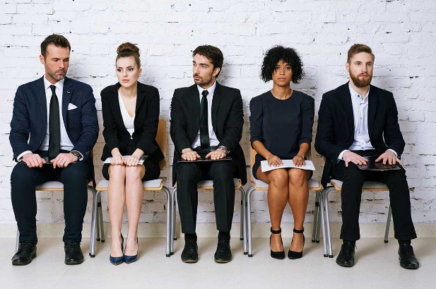 fuenf bewerber auf einen job sitzen vor einer weißen wand