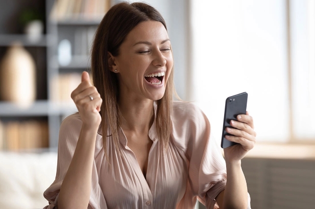 Frau mit einem Handy, die sich freut, weil sie bei einem Social Media Gewinnspiel gewonnen hat
