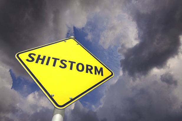 gelbes Schild mit Shitstorm-Aufschrift als Folge von negativen Kommentaren vor bewölktem Himmel