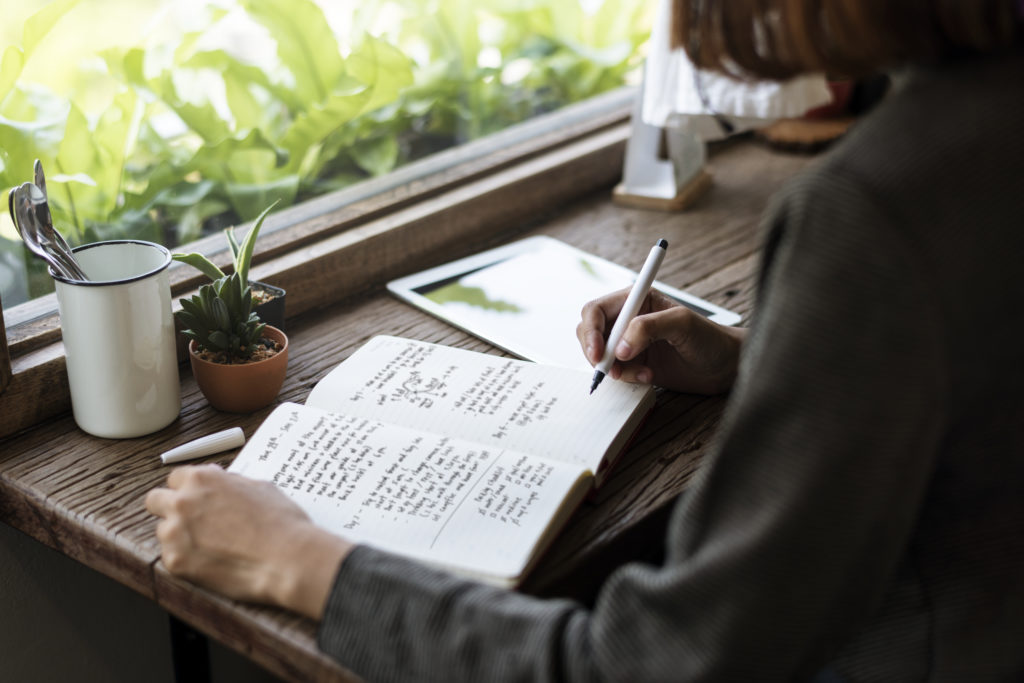 Frau sitzt an einem Schreibtisch und schreibt Notizen für ihr Storytelling in ein Buch